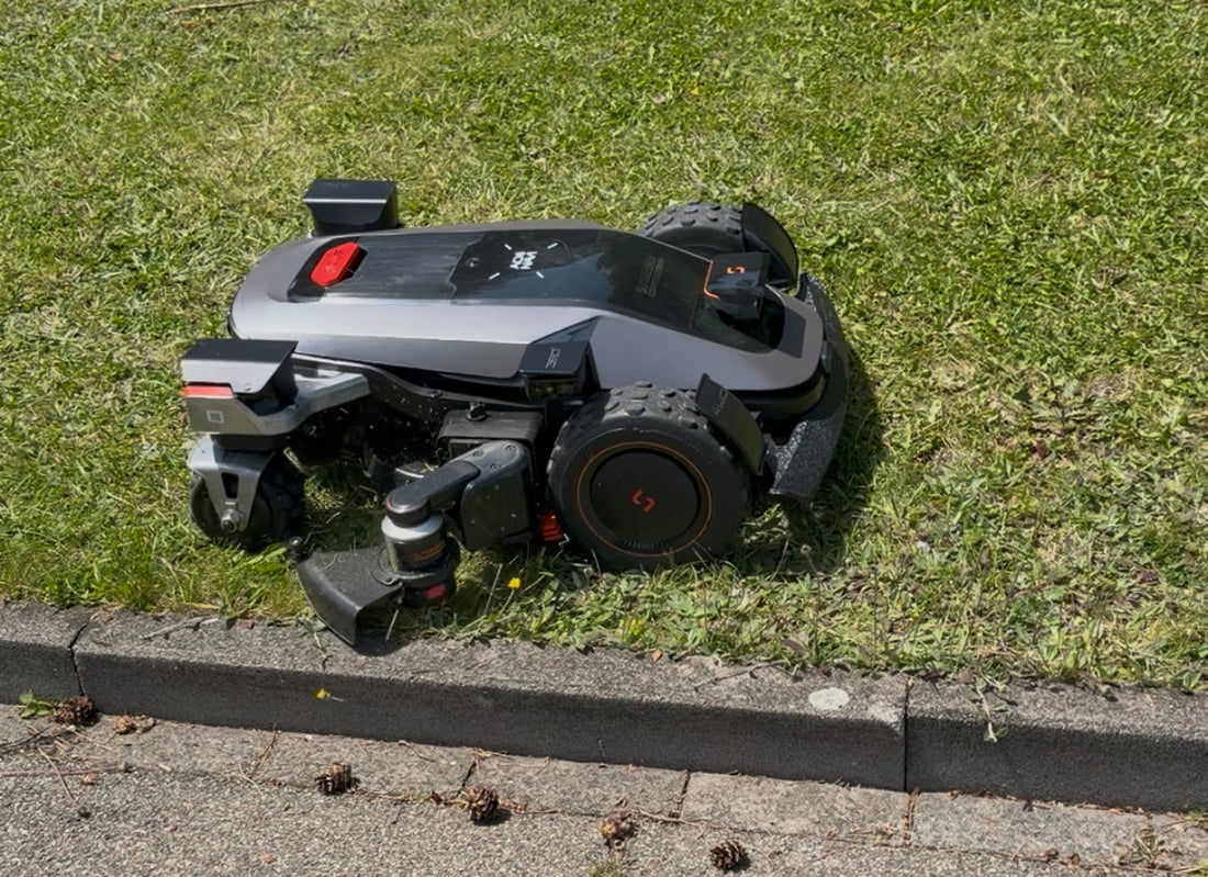 Ein moderner Mähroboter in futuristischem Design mäht einen Rasen direkt an einer Bordsteinkante.