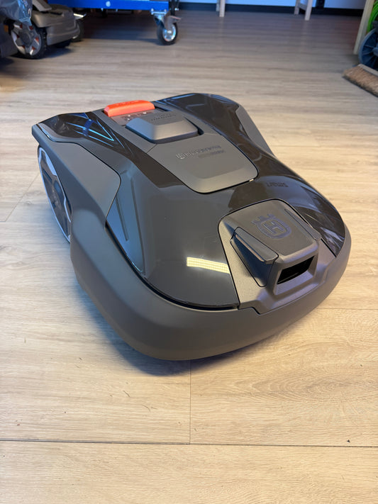 Frontansicht des neuen Husqvarna Automower 308V Rasenroboters (Modell 2026) in dunklem Grau auf hellem Holzboden, deutlich erkennbar ist das Gehäuse der Frontkamera für die visuelle Navigation.